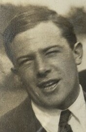 A handsome young man in a suit smiles to camera. 